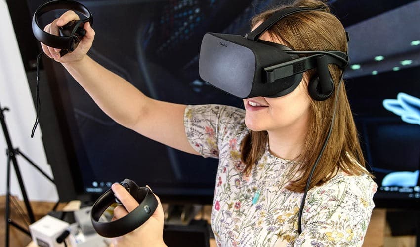 A young woman with a VR headset and controllers in her hands, in front of a large screen